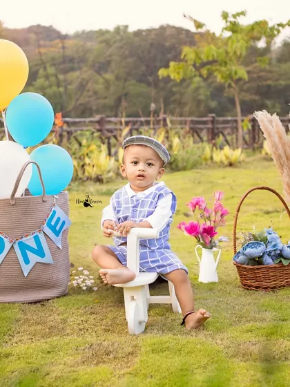 A charming setup for a first birthday picnic, complete with a 'ONE' banner, balloons, and a cute little wooden tricycle prop.