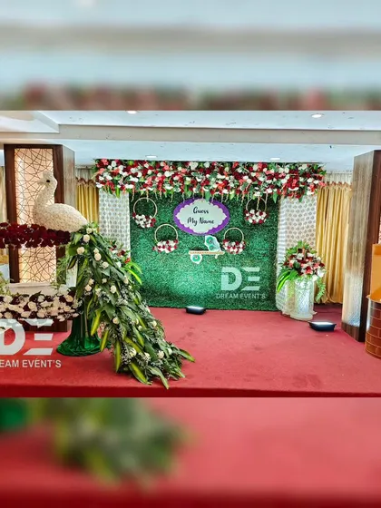 The full stage view for our peacock-themed naming ceremony. The floral peacock sculpture is the star, complemented by a green wall backdrop and a sign that playfully says "Guess My Name?".