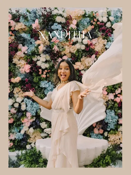 A joyful portrait of the bride with her arms outstretched, her outfit flowing around her. The floral backdrop and her happy expression make this a beautiful, magazine-style shot.