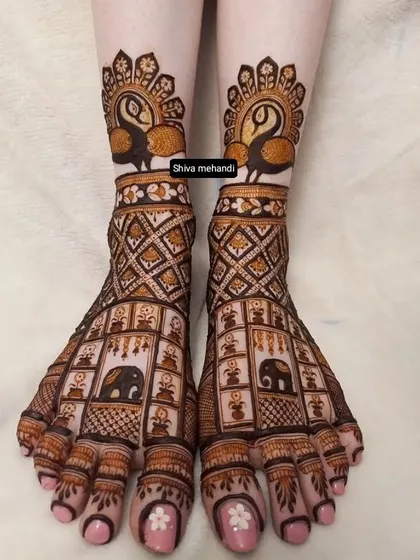 Intricate mehendi on the feet, featuring a grid of elephant motifs on the top and graceful peacocks at the ankles.