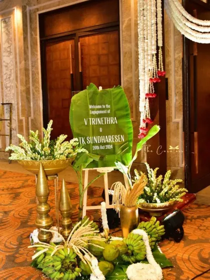 A unique welcome sign crafted on a large leaf, surrounded by brass lamps, coconuts, and banana stalks, immediately immersing guests in the spirit of a traditional South Indian celebration.