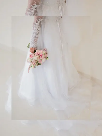 An artistic, framed shot focusing on the bride's beautiful white gown and her bouquet of flowers.