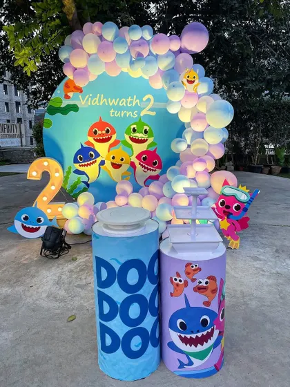 Dive into a Baby Shark themed party for a second birthday. This setup includes a custom backdrop with the whole shark family, marquee light-up numbers, and themed pedestals for the cake.