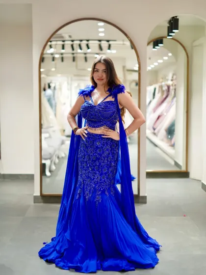 When you walk in wearing this, even silence stares. A full shot of the dramatic blue fish-cut lehenga with a cape, showcasing its powerful silhouette and intricate beadwork.
