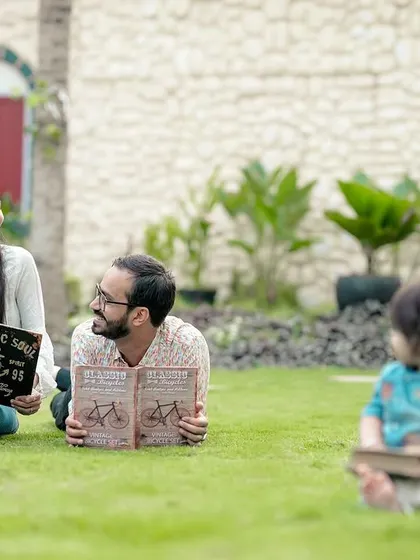 Story time on the lawn. This creative family portrait shows the parents enjoying a book together while their little one has his own, creating a fun and memorable outdoor photo.