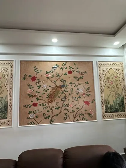 A traditional Indian-themed wallpaper featuring a peacock on a flowering tree, elegantly framed as a triptych on the living room wall.