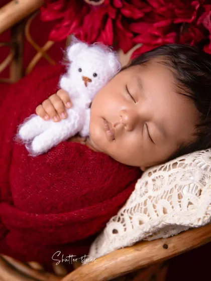 A sweet close-up of the newborn's face, nestled against a lace pillow in the maroon setup.