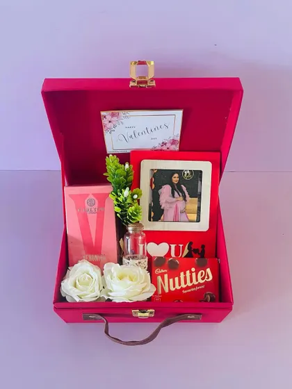 A Valentine's Day combo for her in a pink suitcase box. It includes a photo frame, perfume, and chocolates, making it a complete and thoughtful gift.