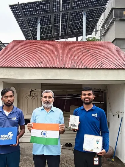 A homeowner and our team stand in front of his house, showcasing the newly installed rooftop solar system and the Indian flag.