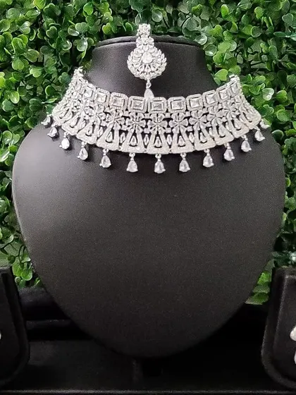 For the modern bride who loves to sparkle, this complete American diamond necklace set is a perfect choice for a reception or cocktail event. It includes a choker, matching earrings, and a delicate maang tikka.