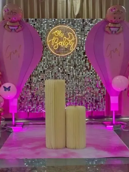 A cute 'Oh Baby' baby shower stage. The backdrop is a silver sequin wall, flanked by hot air balloon-themed decorations made with pink and rose gold balloons.