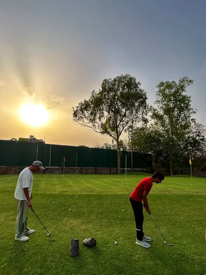Two golfers practice putting against a beautiful sunset, a perfect end to the day.