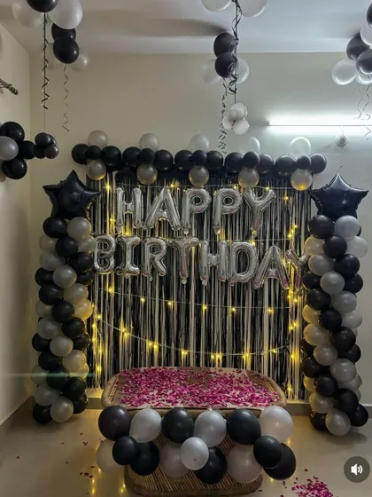 A close-up of the birthday backdrop with a black shimmer curtain, silver foil letters, and black and white balloon pillars.