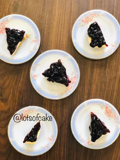An overhead shot of five plates, each with a perfect slice of blueberry cheesecake.