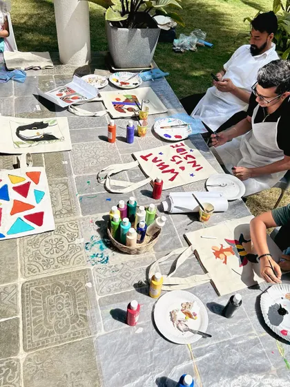An overhead view of the creative chaos at a family paint party. Tote bags and plates are being transformed into colorful works of art.