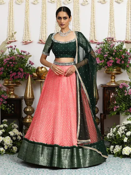 A stunning coral pink pleated silk lehenga paired with a deep green embroidered blouse. The color combination is fresh and vibrant.