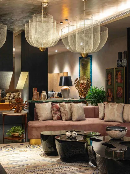 A dusty pink sofa is paired with black lacquer coffee tables and large mesh pendant lights. The room is filled with art, including a painted screen and a Balinese Garuda sculpture, creating a rich, sensory tapestry.