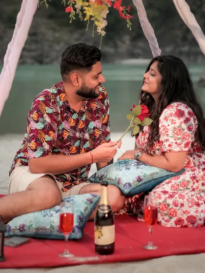 A romantic picnic setup on the banks of the Ganga in Rishikesh, where the groom-to-be offers a rose to his partner. We help you style and create these memorable moments.