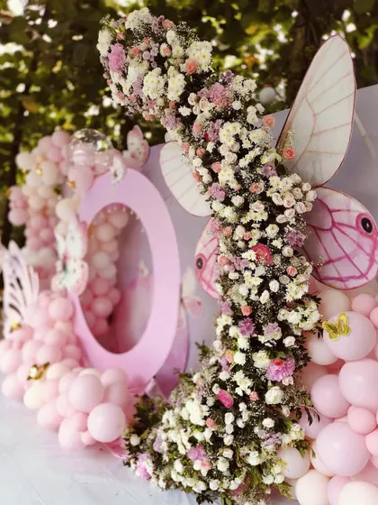 A close-up of a floral and balloon arch for a butterfly-themed party. The combination of fresh flowers and pink balloons creates a soft and beautiful texture.