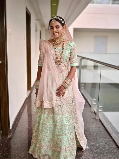 A full-length view of the bride in her mint green and pink pastel lehenga, showing how the soft makeup complements the delicate colors of her outfit.