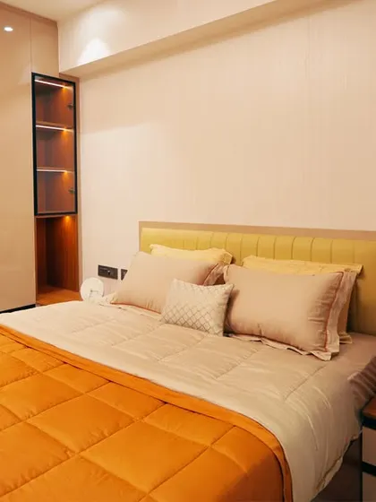 A bright and cheerful bedroom with an orange quilted bedspread. The design includes a full-wall wardrobe with integrated open shelving, providing ample storage and a touch of modern style.