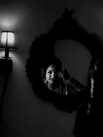 An artistic black and white bridal portrait. The bride is captured in a moment of quiet reflection in the mirror, creating a moody, intimate, and timeless image.