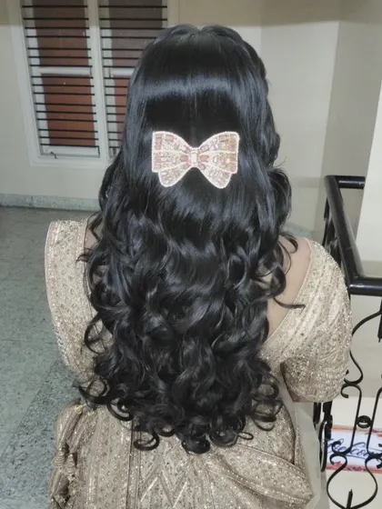 A half-up style with beautiful, flowing curls, accessorized with a delicate, sequined bow.