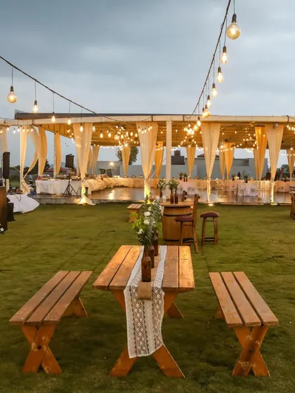An inviting setup for a relaxed Mehendi evening. We used rustic wooden benches and tables, complemented by soft drapes and warm lighting, to create a comfortable and stylish space for guests to mingle.