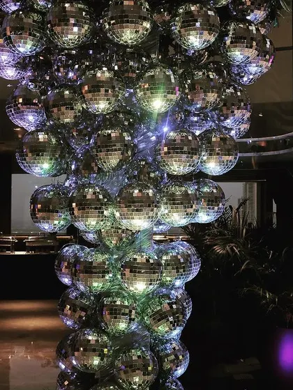 A modern art installation made of dozens of disco balls, creating a sparkling, dynamic column of light perfect for a high-energy party or cocktail hour.