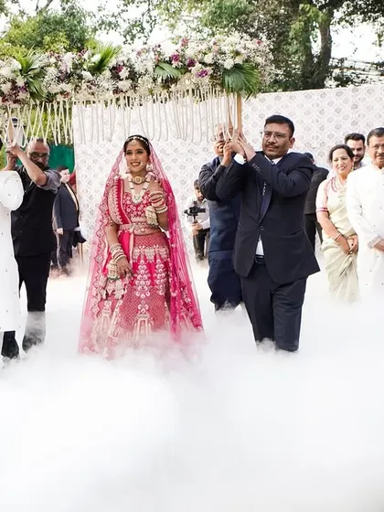 The bride makes her entrance, walking on a cloud of low-lying smoke under a beautiful floral 'phoolon ki chadar'. Professional dancers in traditional attire lead her procession, adding grace and elegance to this special moment.