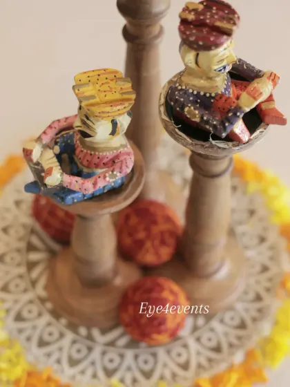 An overhead view of the traditional Rajasthani centerpiece, showing the intricate details of the painted musician figurines and the circular arrangement of marigold petals on a patterned base.