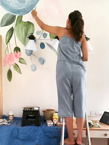 Me on a ladder, adding the final touches to a large floral mural in a client's home. I often work around existing fixtures like lamps to make the art feel truly integrated.