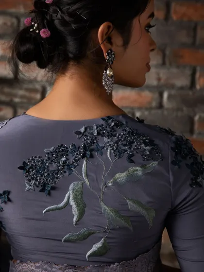A view of the back of this grey organza saree's blouse, highlighting the intricate, nature-inspired embroidery that flows across the shoulders.