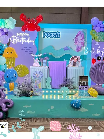 A vibrant "Under the Sea" party for Poorvi. The stage was filled with colorful sea creatures like an octopus and crab, a large seashell, and a beautiful mermaid backdrop.