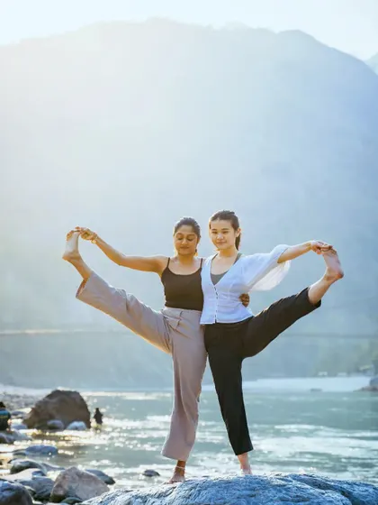 Finding balance together. This partner pose, set against the serene backdrop of Rishikesh, showcases the harmony and stability that can be achieved when you practice with someone else.