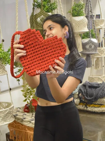 Holding up our bright red, heart-shaped crochet bag. This is a fun and playful design that we absolutely love making. It's a perfect statement piece for Valentine's or any day you want to spread some love.