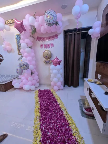 A beautiful welcome home setup combining a pink and white balloon arch with a traditional flower petal runner. This decoration blends modern style with timeless tradition.