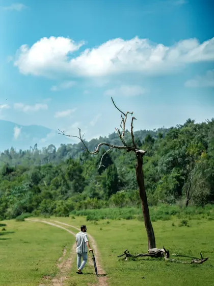A shot of me walking on a dirt path in a green meadow, carrying an umbrella. This image captures the essence of my journey as a wanderer or 'alemari'.