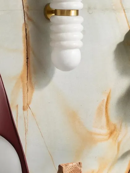 A close-up of the minimalist master retreat, highlighting the unique wall sconce against the marble backdrop. The textures of the maroon bed and grey fabrics add layers of understated elegance.