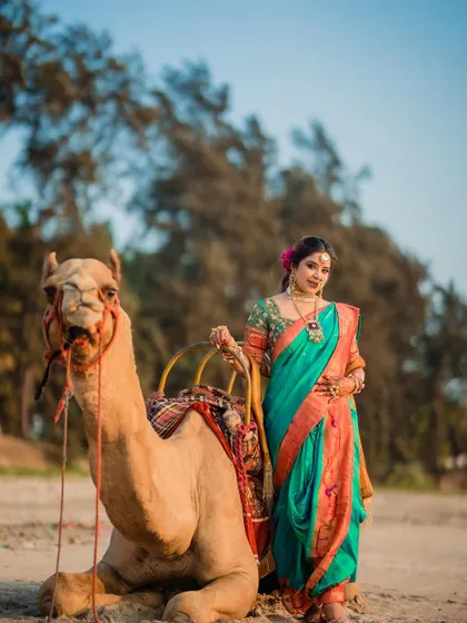 A unique bridal portrait with the bride posing next to a camel on the beach, creating a memorable and artistic shot.