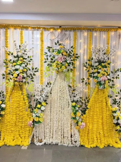 This backdrop for a Haldi or Mehandi ceremony uses curtains of yellow and white flowers. The design creates a beautiful floral wall effect, perfect for elegant and fragrant celebrations.