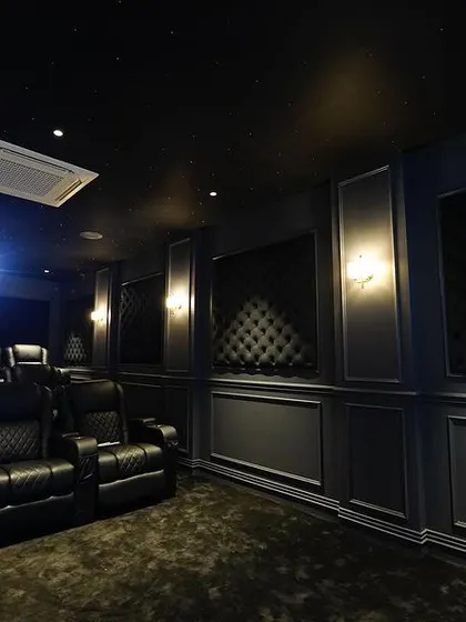 The projector beam cuts through the darkness, highlighting the luxurious details of the room, including the starlit ceiling and the rich, black tufted wall panels.