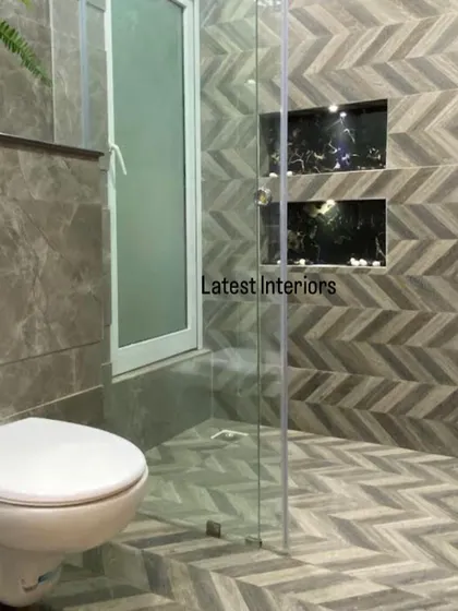 A modern bathroom with a unique chevron-patterned tile on the floor and shower wall. The glass partition and built-in niches create a sleek and functional shower area.