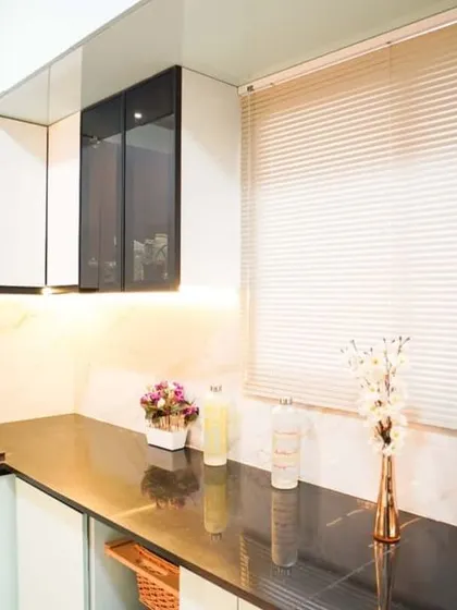 This kitchen design features a striking contrast between glossy white cabinets and a black countertop. The marble-veined backsplash adds a touch of elegance, while the window with blinds allows for natural light control.