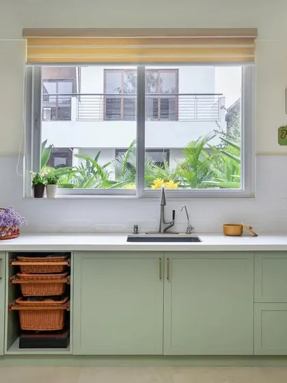 The finished sage green kitchen, showcasing the sink area with a large window that floods the space with natural light.
