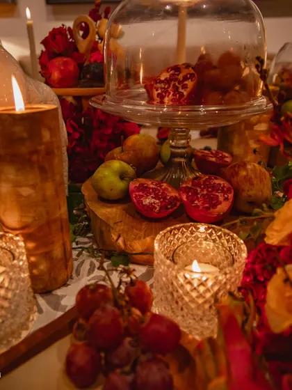 A detail shot showing halved pomegranates and fresh grapes scattered amongst the decor. Incorporating edible elements adds a sense of abundance and sensory delight to the tablescape.