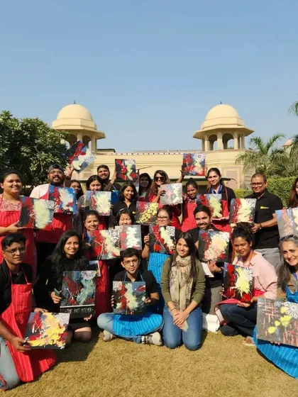 A fantastic group photo from an outdoor art event with the Central Square Foundation. Everyone is proudly holding up the abstract paintings they created, showcasing a wide range of color and expression.