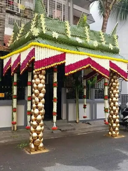 A unique chapra design with pillars made from stacked coconuts painted gold. The roof is decorated with red and white flower garlands, creating a rich and festive look.