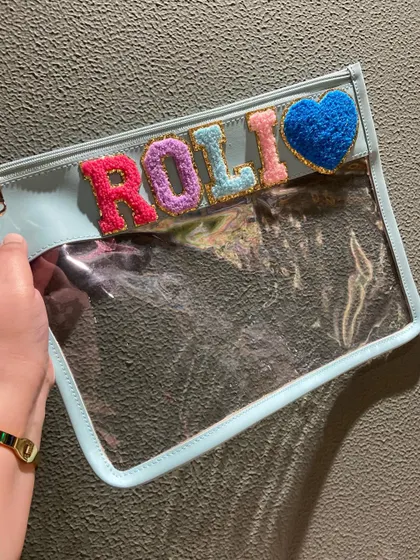 A beautiful light blue clear pouch, personalised with a name and a fuzzy heart patch. It's a sweet and stylish way to stay organised.