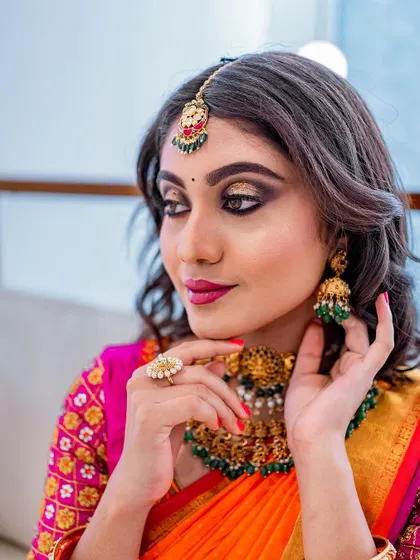 A close-up on the makeup details. Note the blended gold and black eyeshadow, the precise maang tikka placement, and the elegant jhumkas.